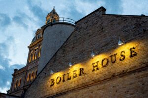 Edificio industriale storico in mattoni con scritta illuminata 'BOILER HOUSE' e ciminiera sullo sfondo - architettura che ha ispirato la rivoluzione del clubbing underground