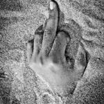 Mano che emerge dalla sabbia con il dito medio alzato, fotografia in bianco e nero